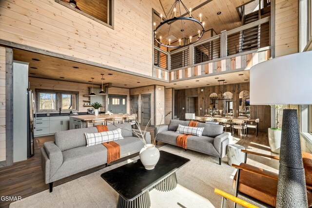 living area featuring wooden ceiling, wooden walls, wood finished floors, a towering ceiling, and an inviting chandelier