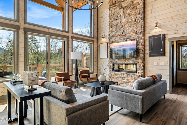 living area featuring wooden walls, a chandelier, a stone fireplace, and wood finished floors