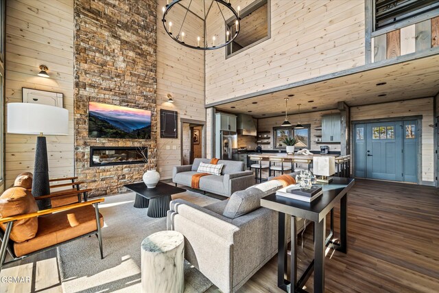 living area with dark wood-style floors, a fireplace, wooden walls, and an inviting chandelier