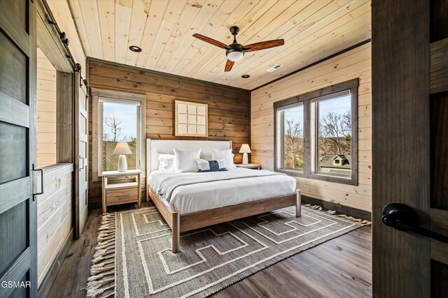 bedroom featuring wooden ceiling, a barn door, wooden walls, and wood finished floors