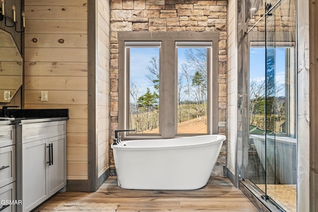 bathroom featuring wooden walls, vanity, a freestanding bath, and wood finished floors