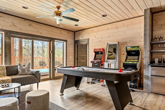 rec room featuring light wood-style floors, wooden ceiling, wooden walls, and a ceiling fan