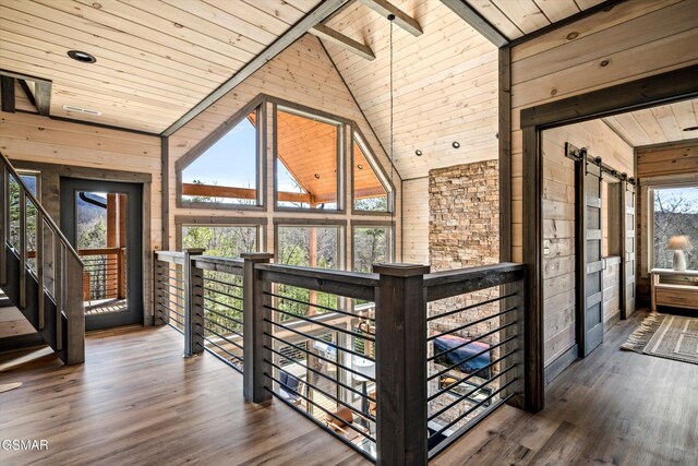 hall featuring a barn door, wooden walls, wood ceiling, wood finished floors, and high vaulted ceiling