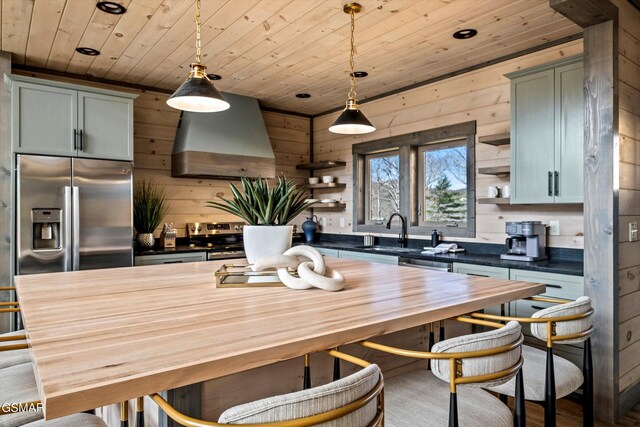 kitchen featuring stainless steel appliances, a sink, wall chimney range hood, and open shelves