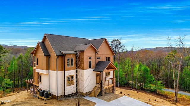 exterior space with roof with shingles, a mountain view, a view of trees, and central air condition unit