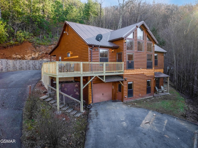 log-style house with a garage, metal roof, a forest view, and aphalt driveway