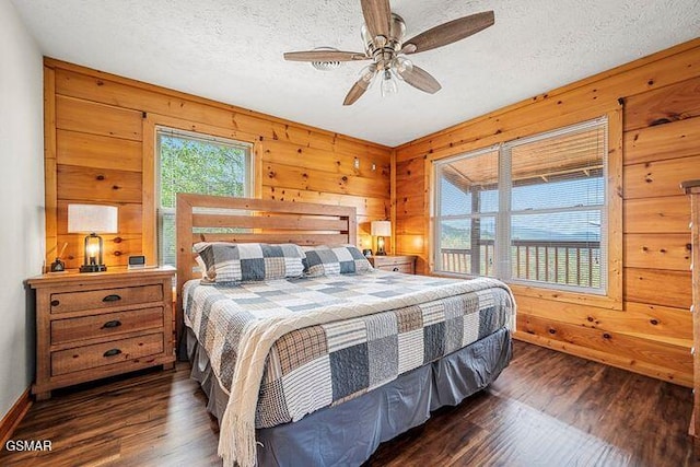 bedroom featuring dark wood-style flooring, baseboards, ceiling fan, wooden walls, and a textured ceiling
