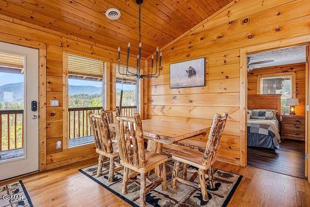 dining space featuring wood walls, vaulted ceiling, light wood-style flooring, and visible vents