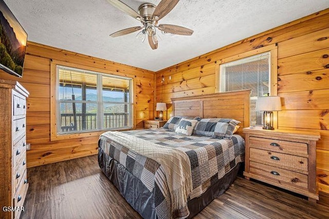 bedroom featuring wooden walls, dark wood-style flooring, a textured ceiling, and ceiling fan