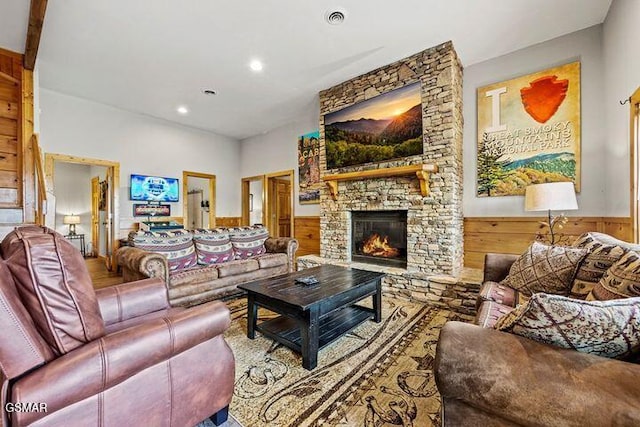 living room with visible vents, wood walls, wainscoting, a stone fireplace, and recessed lighting