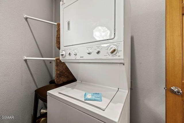 laundry area with laundry area, a textured wall, and stacked washer / dryer