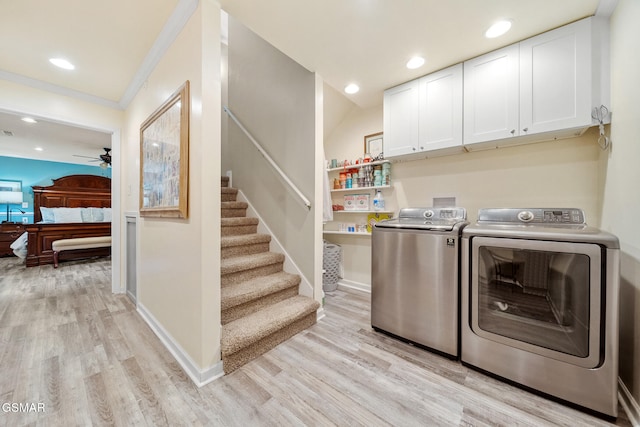 clothes washing area with cabinet space, light wood-style floors, a ceiling fan, baseboards, and washing machine and dryer