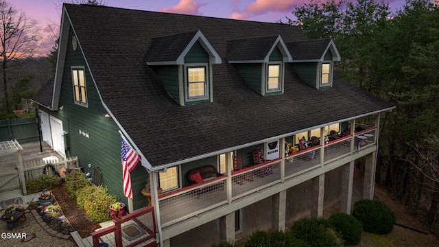 rear view of house with roof with shingles, fence, and a balcony