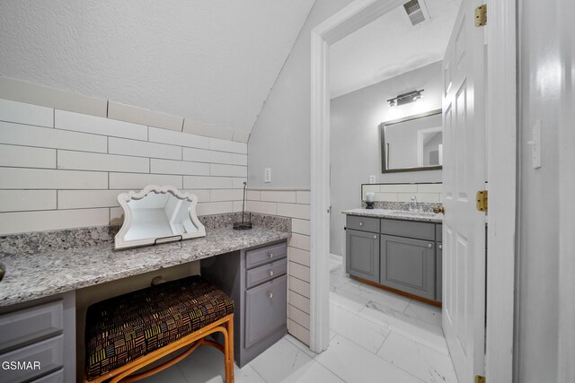 bathroom featuring visible vents, tile walls, vanity, marble finish floor, and lofted ceiling