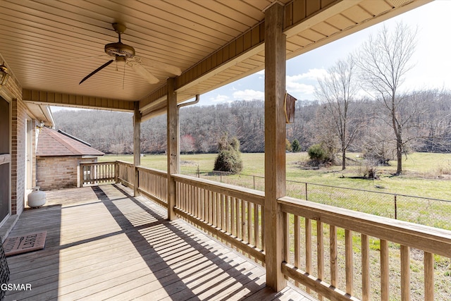 wooden deck featuring a forest view, a yard, a ceiling fan, and fence