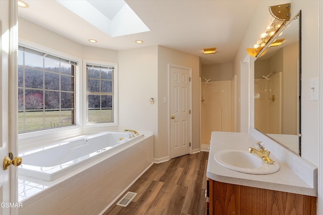 bathroom featuring wood finished floors, visible vents, a skylight, a shower, and a garden tub