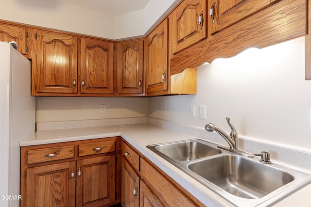 kitchen with brown cabinetry, light countertops, freestanding refrigerator, and a sink