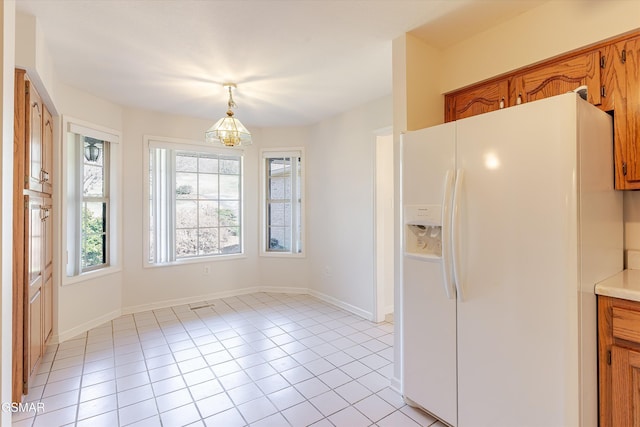 kitchen with light tile patterned floors, white fridge with ice dispenser, brown cabinetry, and light countertops