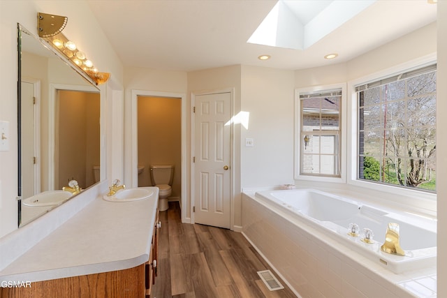 full bath with a bath, wood finished floors, visible vents, a skylight, and toilet