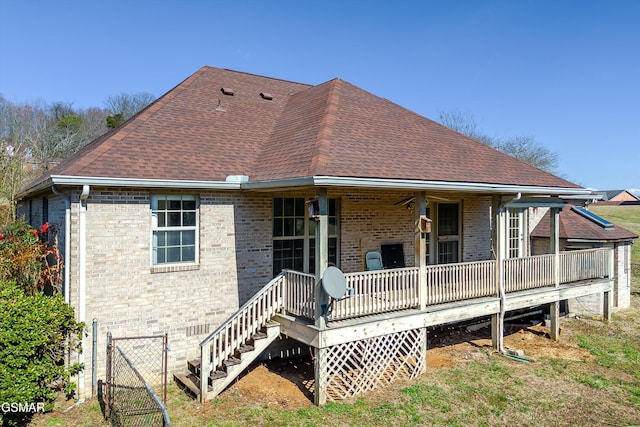 rear view of property featuring brick siding, a porch, roof with shingles, and a gate