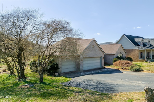 view of front of property featuring aphalt driveway, an attached garage, brick siding, and a front yard