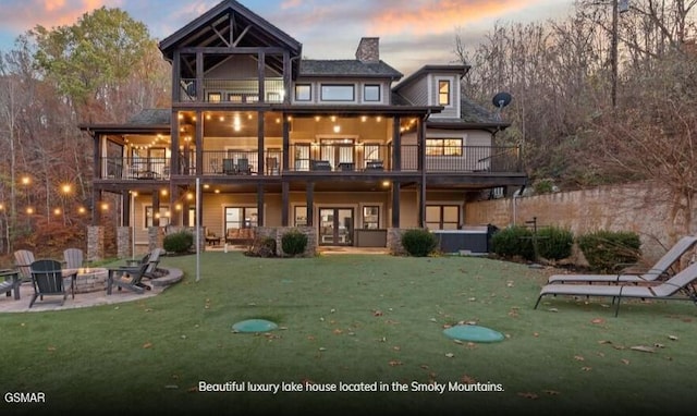 back house at dusk with a lawn, a patio area, a balcony, and an outdoor fire pit