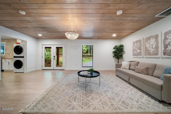 living area featuring stacked washer / drying machine, wood ceiling, light wood finished floors, french doors, and baseboards