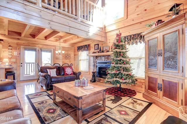 living room featuring a stone fireplace, a notable chandelier, light hardwood / wood-style floors, wooden walls, and wood ceiling