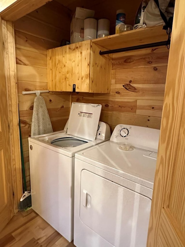 washroom featuring light wood-type flooring, separate washer and dryer, and wooden walls