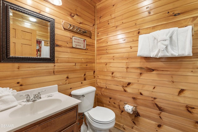 bathroom featuring toilet, vanity, and wooden walls