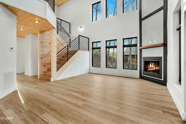 unfurnished living room featuring a towering ceiling, wooden ceiling, and light hardwood / wood-style floors