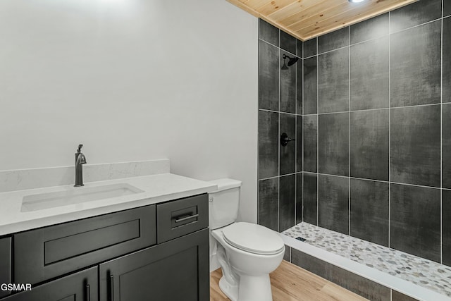 bathroom with wood ceiling, toilet, vanity, a tile shower, and hardwood / wood-style flooring