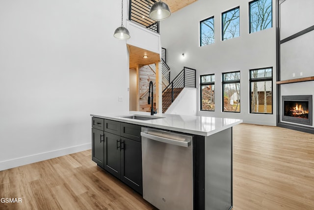 kitchen featuring sink, decorative light fixtures, a towering ceiling, stainless steel dishwasher, and a kitchen island with sink