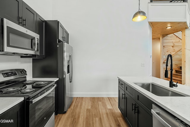 kitchen with light stone countertops, light hardwood / wood-style flooring, decorative light fixtures, stainless steel appliances, and sink