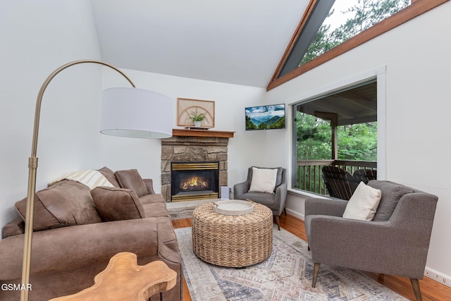 living area with high vaulted ceiling, a stone fireplace, wood finished floors, and baseboards