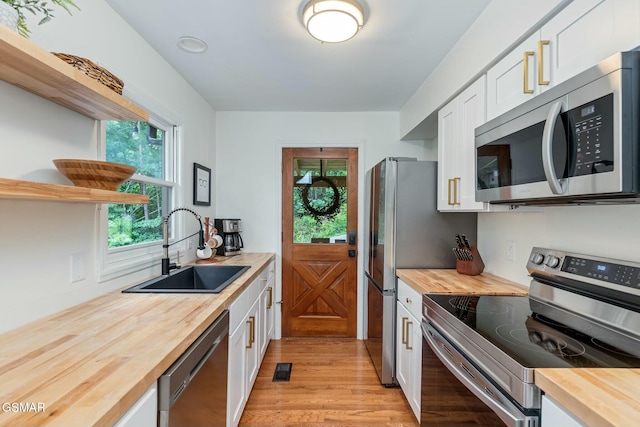 kitchen with butcher block counters, light wood-style flooring, stainless steel appliances, white cabinetry, and a sink