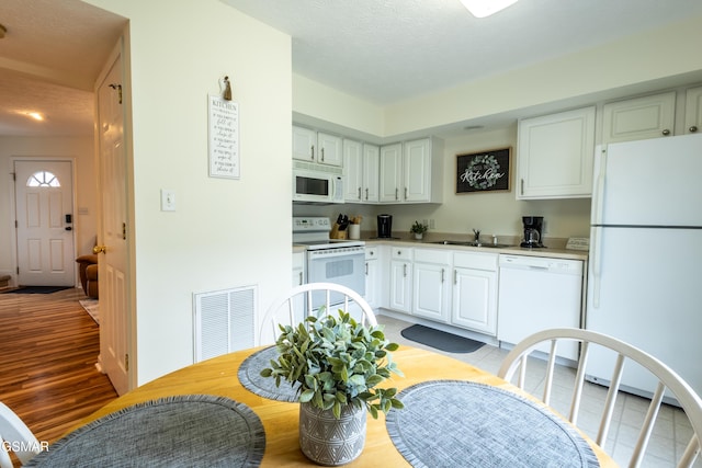kitchen with white cabinetry, a sink, visible vents, light countertops, and white appliances