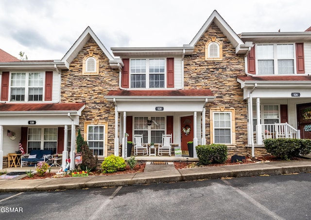 view of property featuring uncovered parking, stone siding, and covered porch