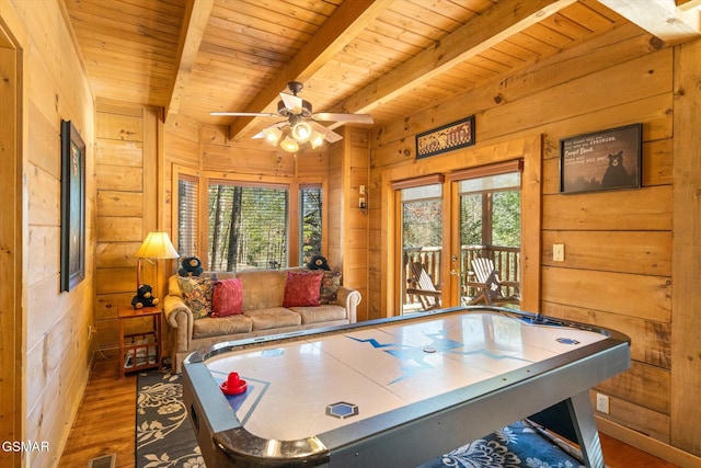 game room featuring beam ceiling, a healthy amount of sunlight, and wood walls