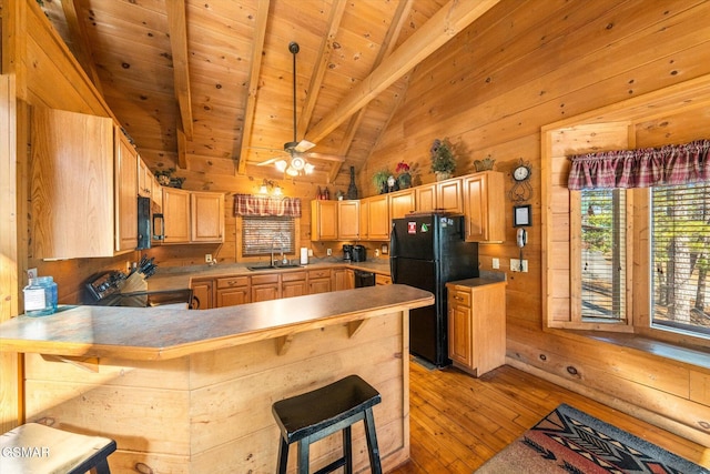 kitchen featuring electric range oven, black fridge, kitchen peninsula, a kitchen bar, and sink