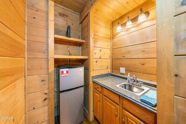 kitchen featuring wooden ceiling, sink, wood walls, and stainless steel refrigerator