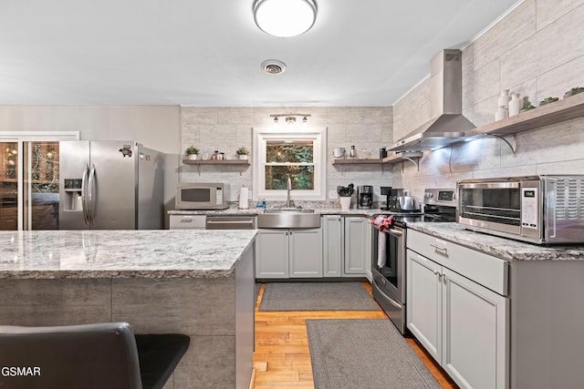 kitchen featuring light stone counters, wall chimney range hood, sink, and appliances with stainless steel finishes