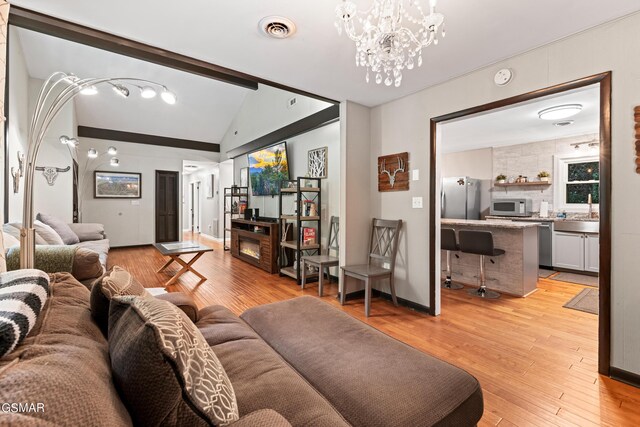 living room featuring lofted ceiling with beams, light wood-type flooring, sink, and a chandelier