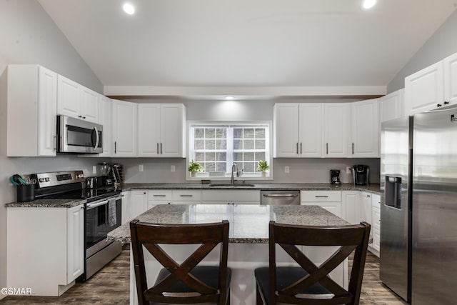 kitchen featuring lofted ceiling, appliances with stainless steel finishes, a kitchen bar, and a sink