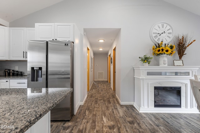 kitchen with visible vents, vaulted ceiling, dark stone counters, stainless steel fridge, and a glass covered fireplace