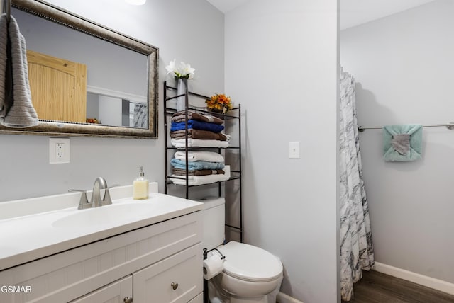 bathroom with curtained shower, toilet, wood finished floors, vanity, and baseboards