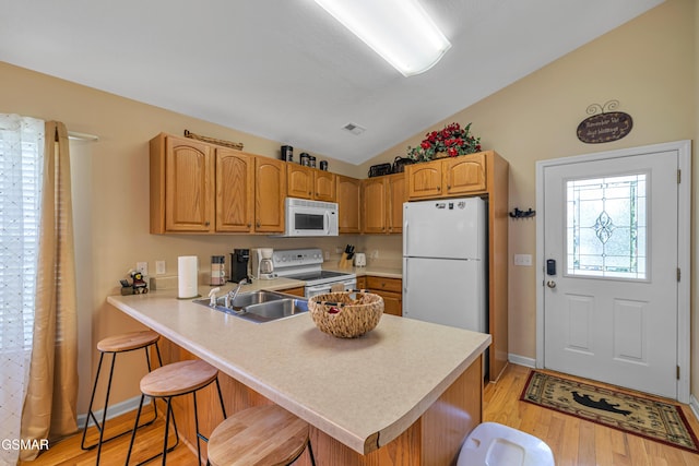 kitchen with white appliances, lofted ceiling, a sink, light wood-style flooring, and a breakfast bar