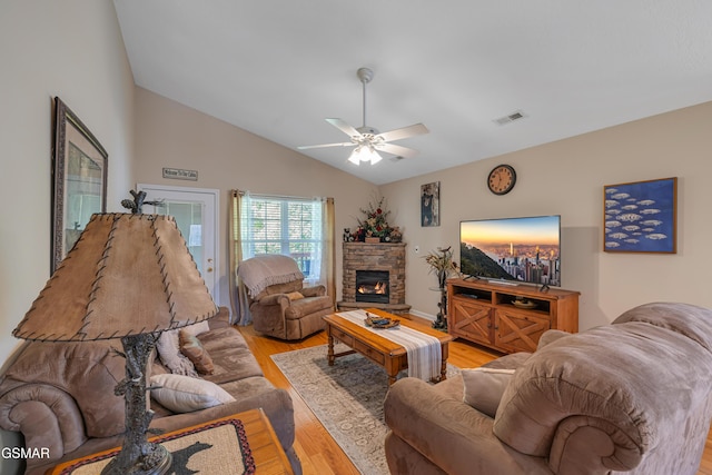 living area with light wood finished floors, a ceiling fan, a stone fireplace, and high vaulted ceiling