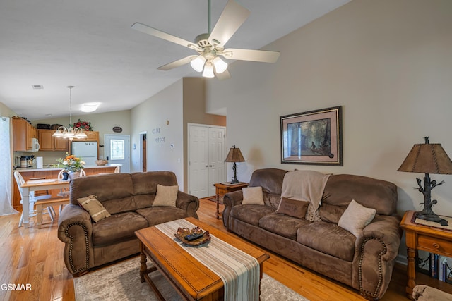 living room featuring lofted ceiling, a chandelier, light wood finished floors, and a ceiling fan