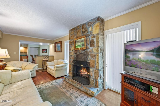 living room with light wood-type flooring, ornamental molding, a textured ceiling, and a stone fireplace